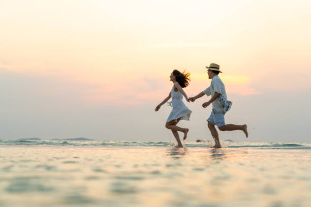 coppia asiatica felice che gioca in acqua di mare sulla spiaggia tropicale dell'isola al tramonto estivo - beach women joy sand foto e immagini stock