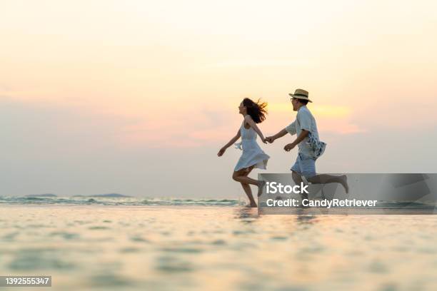 Happy Asian Couple Playing In Sea Water On Tropical Island Beach At Summer Sunset Stock Photo - Download Image Now