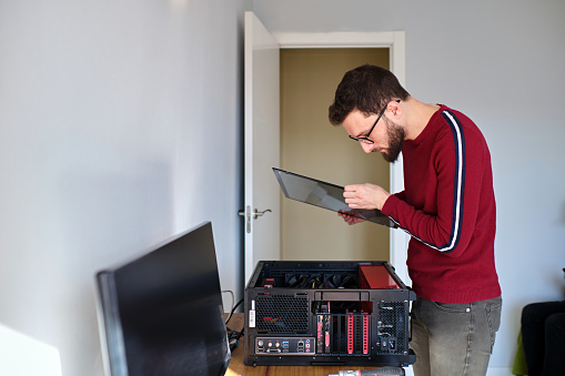 Side view of a young man opening his pc to improve it at home.