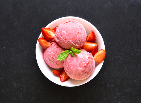 Strawberry ice cream in bowl on dark stone background. Top view, flat lay