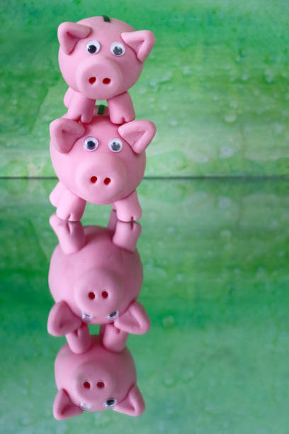 Stock photo showing a close-up view of two piggy banks stacked on top of each other on mirrored surface. This is a family finances and savings concept picture.