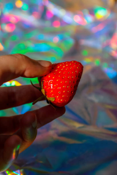 Defocus close-up hand holding ripe red strawberry on modern hologram background. Fruits and berries. Harvest and crop concept. Organic. Gradient. Out of focus