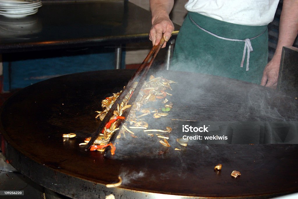 Mongolian BBQ A picture of a chef cooking a meal on a 'Mongolian BBQ' grill. Focus is on the food bwteen the tongs. Barbecue Grill Stock Photo