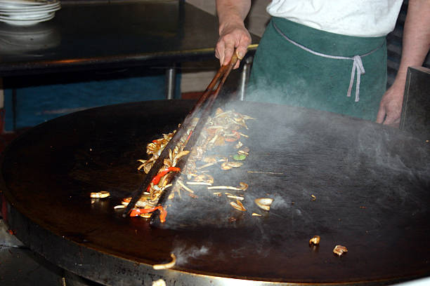 Mongolian BBQ A picture of a chef cooking a meal on a 'Mongolian BBQ' grill. Focus is on the food bwteen the tongs. mongolian ethnicity stock pictures, royalty-free photos & images