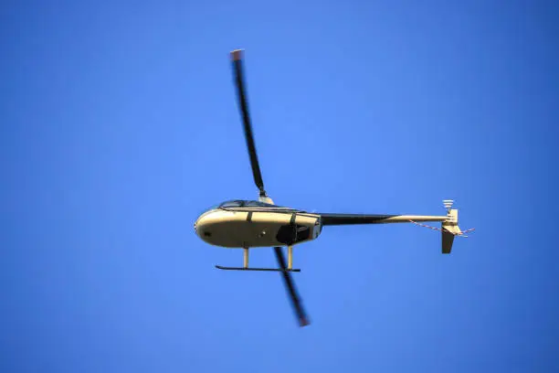 The helicopter Robinson R44 flies in the blue sky