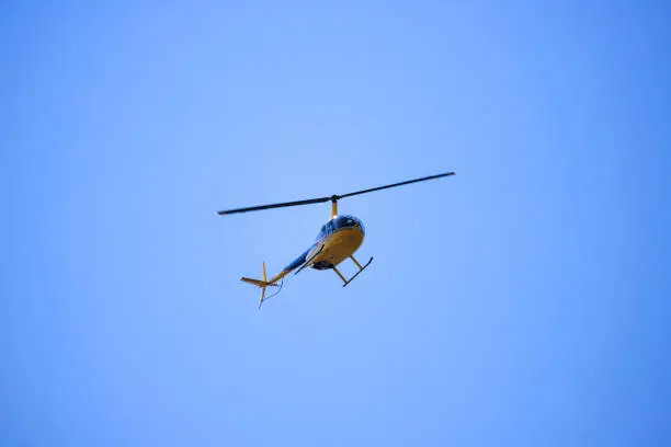 The helicopter Robinson R44 flies in the blue sky