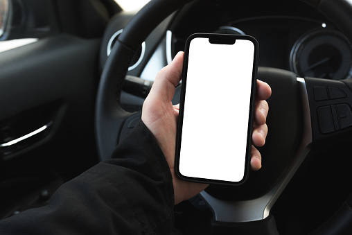 Male driver using smartphone in the car, blank white screen of mobile device as copy space, selective focus