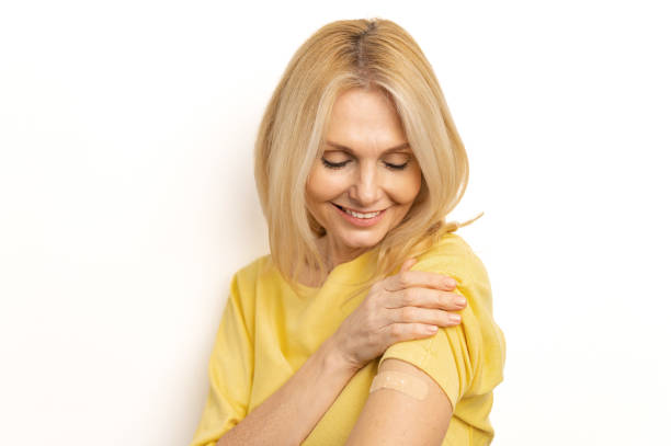 istock Happy mature lady on white empty blank studio background looking at her hand, smiling and showing arm after vaccine injection. Coronavirus, Covid-19, flu vaccination and immunization 1392568481