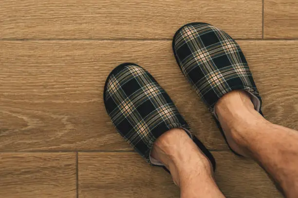 Male feet wearing plaid slippers in bathroom, top view with copy space