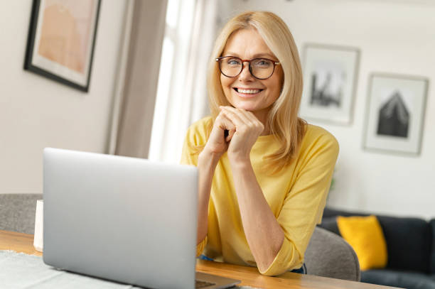 istock Charming senior elderly woman spends leisure time in networks on the computer, texting messages, watching movies. The mature lady works remotely with a laptop sitting at the table 1392568741