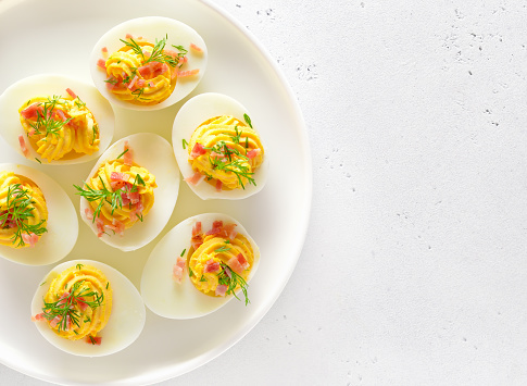 Stuffed eggs with egg yolk, bacon, mustard on plate over light stone background with free text space. Top view, flat lay.