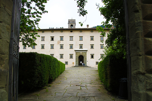 The photo was taken at the entrance of the Vallombrosa Abbey, across the gate, on a late spring day. It shows the road leading to the entrance of the building and passing across the gardens.