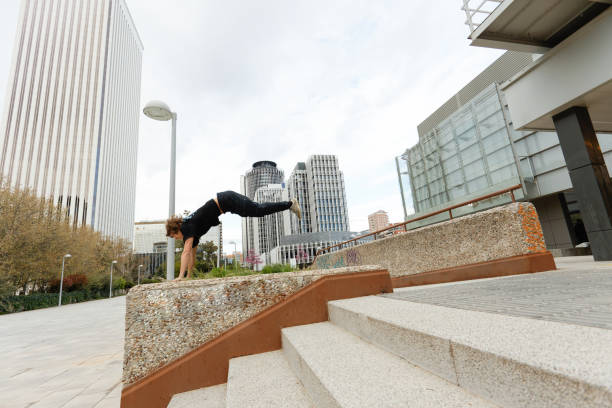 Side view of a young man doing parkour jumping from a railing and propelling himself with his hands resting on grass.