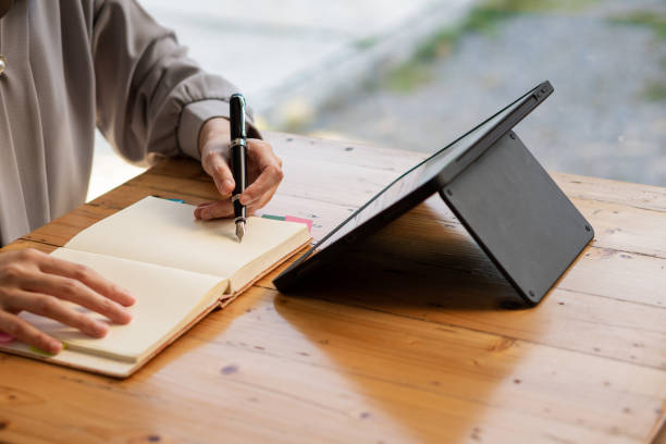 istock a businesswoman holding a pen and writing on a notebook using a tablet while working Portrait of a freelance woman with modern digital devices spending her free time working on web projects. 1392569706
