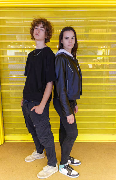 istock Young people posing standing back to back looking at camera against a yellow shutter. 1392570460