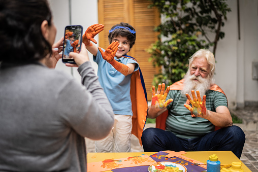 Woman taking photos of boy and grandfather showing hands with paint