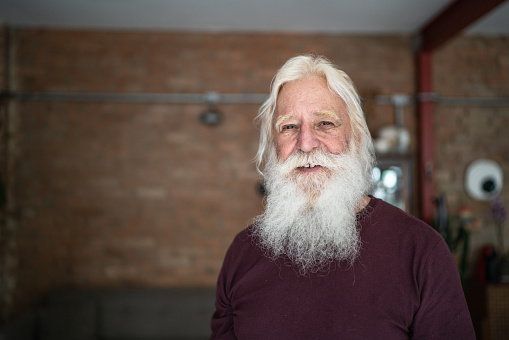 Smiling handsome people white-haired standing in front of a white wall looking at camera. Midsection portrait of attractive and joyful old man
