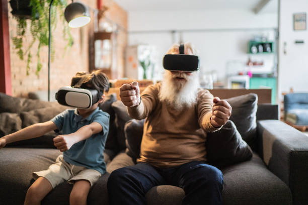 abuelo y nieto jugando con gafas de realidad virtual en casa - diferencia entre generaciones fotografías e imágenes de stock