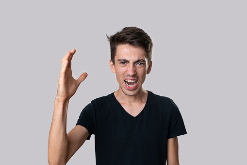 portrait of a young man in a black T-shirt, serious, angry and shouting angrily. Studio shooting, gray background.