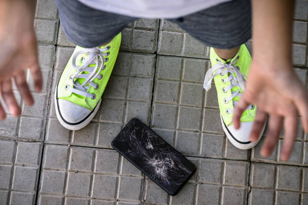 niño pequeño rompiendo el teléfono celular, dispositivo caído al suelo y pantalla destrozada, sin concierto, niño descuidado, película protectora de teléfono inteligente agrietada - dropped call fotografías e imágenes de stock