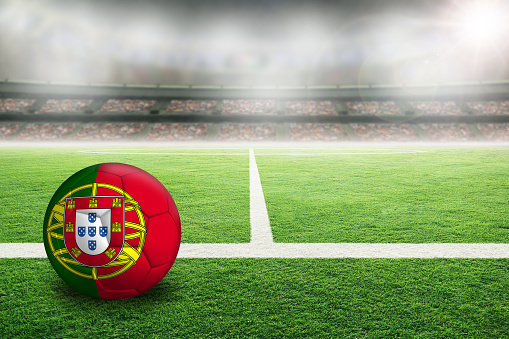 Football in brightly lit outdoor stadium with painted flag of Portugal. Focus on foreground and soccer ball with shallow depth of field on background and copy space.