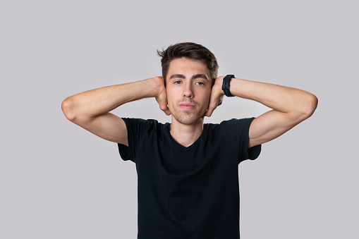 Portrait of a young man in a black shirt, looking at the front, serious, does not want to hear, does not wonder, His hands are in his lapels. Studio shooting, gray background.