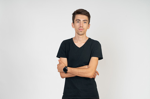 Front-facing, solemn, expressionless, with crossed arms, portrait of a young man in a black T-shirt. Studio shooting, gray background.