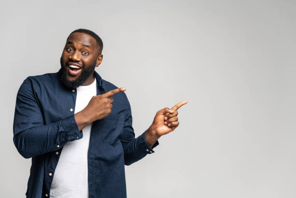 istock Cheerful overjoyed African-American guy points fingers at empty copy space 1392577188