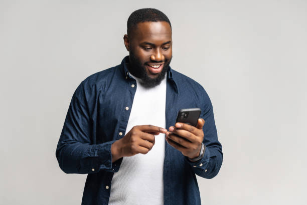 istock Joyful African-American man using smartphone isolated on grey 1392577286