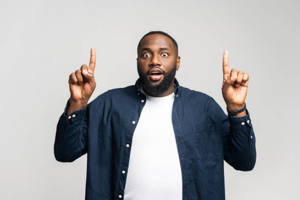 istock Amused African-American man points index fingers up, looking at the camera 1392578679