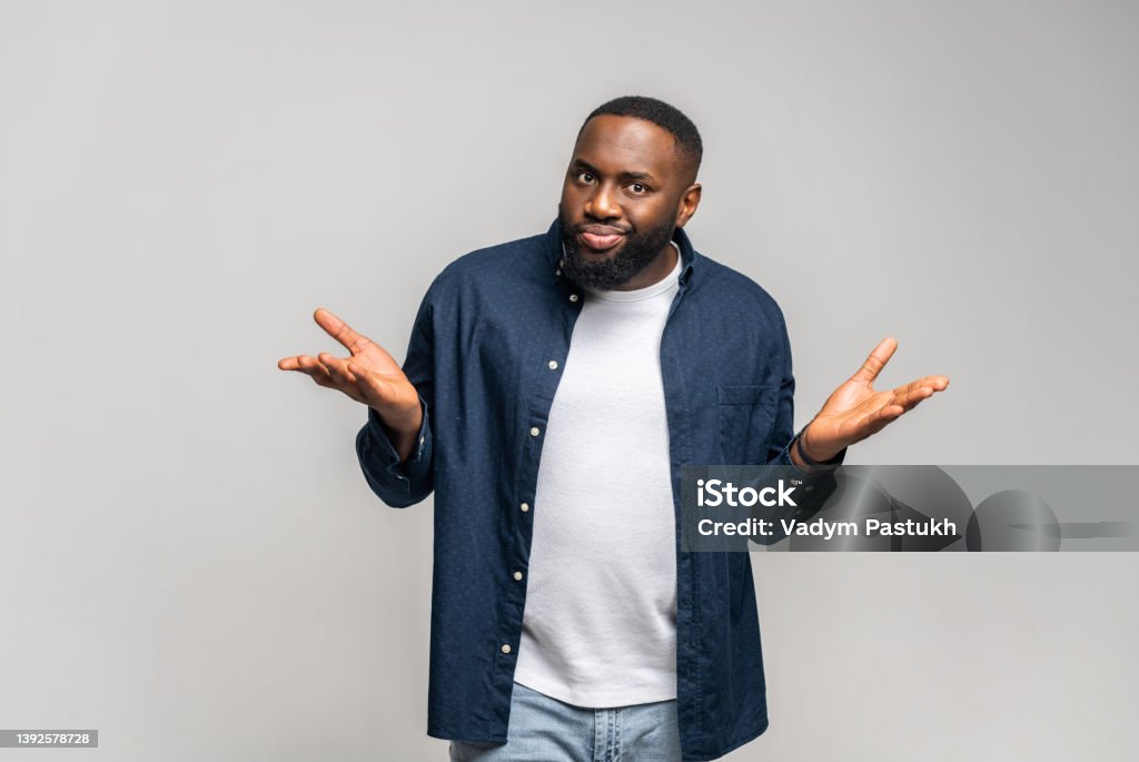 African-American guy shrugging shoulders, asking what is the problem Uncertain African-American guy shrugging shoulders, asking what is the problem, holding arms out, looking at the camera isolated on gray background Men Stock Photo