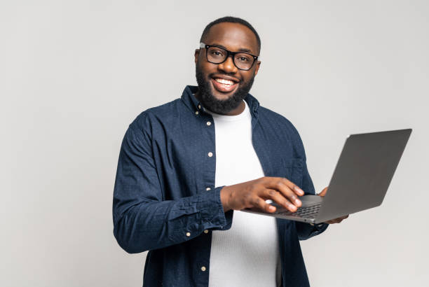 istock Smiling african man using laptop, standing at grey backdrop 1392578912