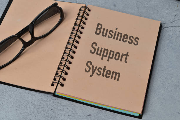 istock Top view of eyeglasses and notebook written with BUSINESS SUPPORT SYSTEM. 1392578913