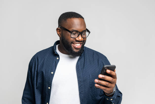 istock Portrait of cheerful young black guy sending message on mobile phone over white 1392578956