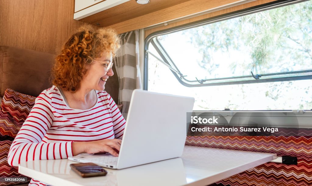 A woman works with a laptop computer inside a caravan. Mature Women Stock Photo