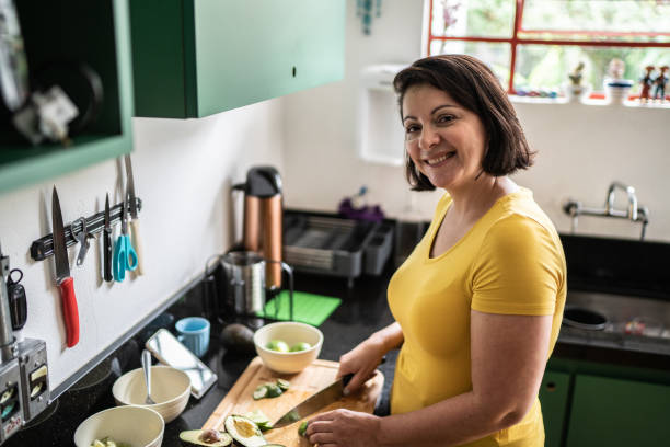 retrato de uma mulher madura cortando comida em casa - guacamole mexican cuisine avocado food - fotografias e filmes do acervo