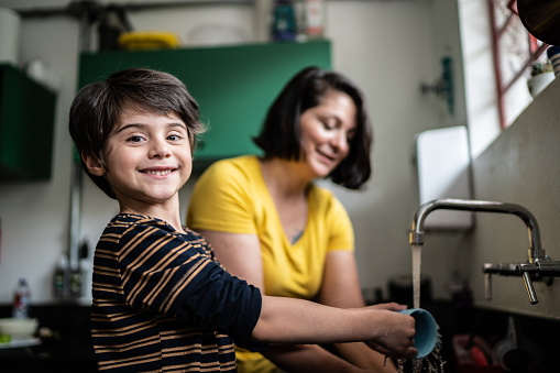 Portrait of happy boy washing dishes with mother at home