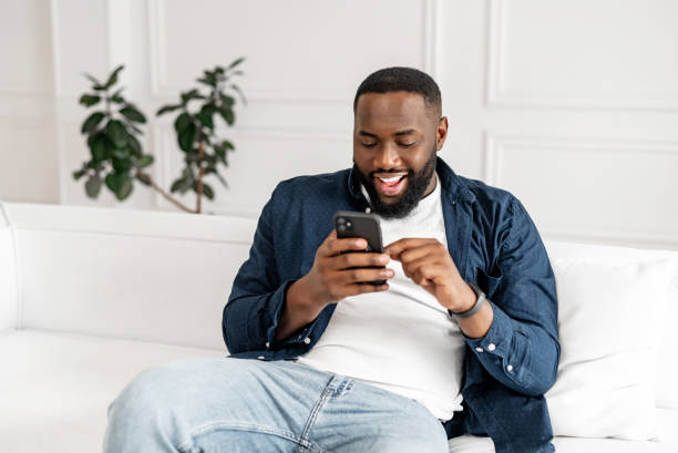 istock Excited young African-American bearded guy in casual using smartphone 1392582290