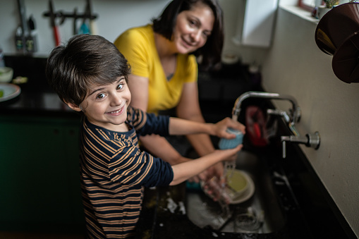Boy washing dishes with mother at home