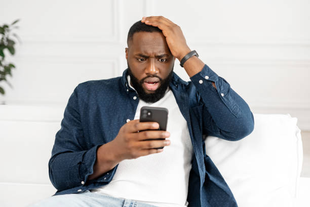 istock Worried young African-American bearded guy staring at smartphone screen 1392582320