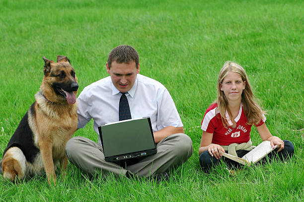 Man, girl and dog sitting in the grass Man with laptop, girl with a book and german shepherd sitting in the grass 2004 2004 stock pictures, royalty-free photos & images