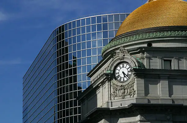 A clock tower with a gold dome, in front of a modern building. The dome has a scalloped texture.