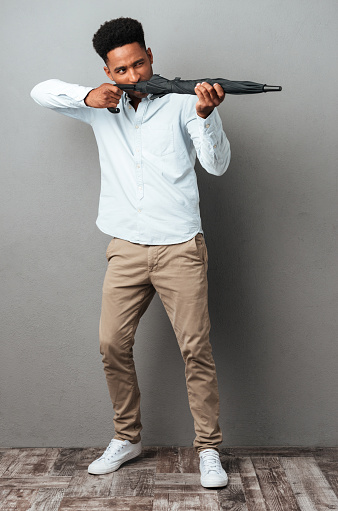 Young afro american man using umbrella like a gun and shooting isolated over gray background