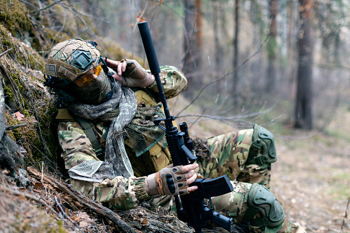 Photo of a special forces soldier during a clash in the forest. He calls his group's support on the walkie-talkie. The concept of modern military operations.