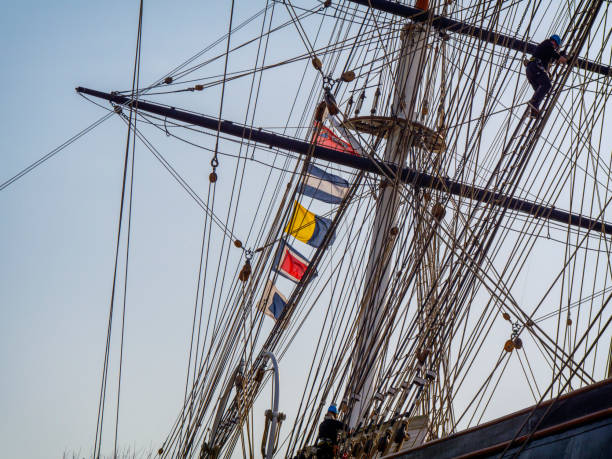 Two people climbing the rigging on the Cutty Sark sailing ship in Greenwich, London. The signal flags are a method of identifying the ship, plus the Red Ensign.