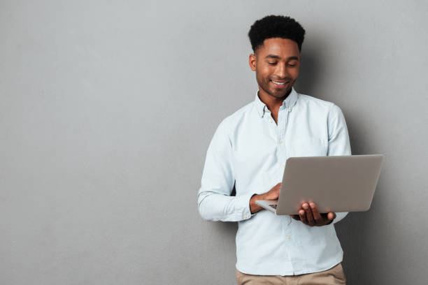 Young smiling african man standing and using laptop stock photo