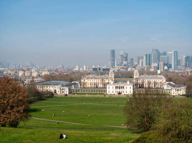 London skyline from Greenwich On a misty yet sunny day, a view from the hill on which stands the Royal Observatory looking over to London’s Docklands (Canary Wharf) in the background and the Old Royal Naval College (now the University of Greenwich), the Queen’s House and National Maritime Museum in the middle distance. Even though it is still March and there are no leaves upon the trees, the weather is warm enough for people to enjoy sitting on the grass, taking in the magnificent view. queen's house stock pictures, royalty-free photos & images
