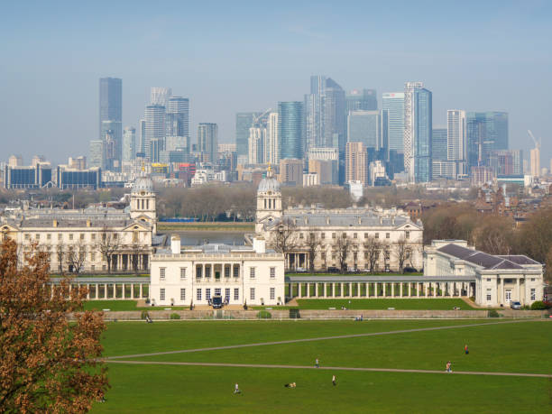 On a misty yet sunny day, a view from the hill on which stands the Royal Observatory looking over to London’s Docklands (Canary Wharf) in the background and the Old Royal Naval College (now the University of Greenwich), the Queen’s House and National Maritime Museum in the middle distance. Even though it is still March and there are no leaves upon the trees, the weather is warm enough for people to enjoy Greenwich Park.