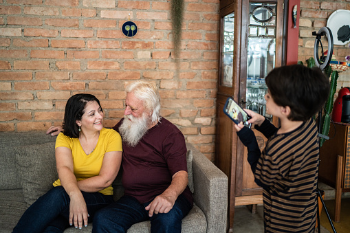 Boy taking picture of mother and grandfather on smartphone at home