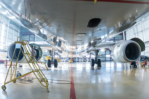 White passenger aircraft in the hangar. Bottom view of the airplane under maintenance. Checking mechanical systems for flight operations